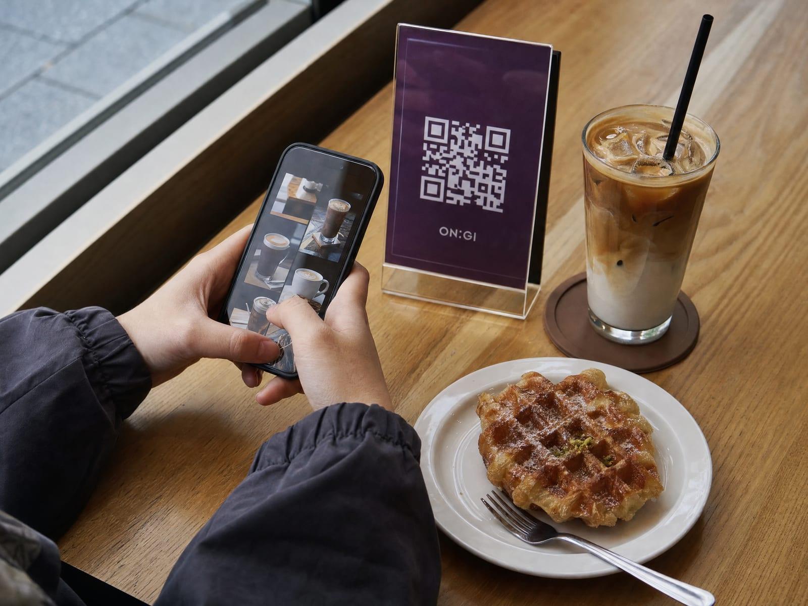 카페 테이블에서 QR 주문 화면을 들고 있는 고객